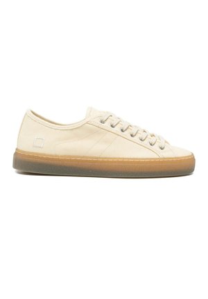 Beige lage canvas sneaker met beige veters en een doorzichtige bruine rubberen zool, gezien van opzij op een witte achtergrond.