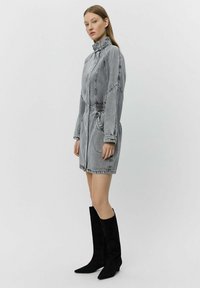 Grå denimklänning med hög krage, elastisk midja och sidofickor; använd med knähöga stövlar i svart mocka.