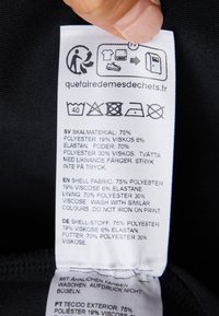 Kledinglabel met zorginstructies en stofsamenstelling in meerdere talen. De tekst bevat symbolen voor wassen en drogen.