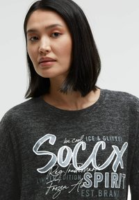 Dark gray long-sleeve shirt with a round neckline, featuring white graphic text "SOCCX" and other decorative elements in varying fonts.