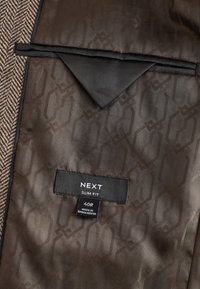 Braunes Fischgrätgewebe mit einem glatten, gemusterten Futter. Verfügt über ein Etikett mit der Aufschrift "NEXT SLIM FIT" und der Größe 40R.