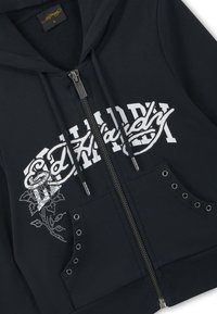 Zwarte hoodie met rits, witte gestileerde "Ed Hardy" tekst, rozenontwerp van strass-steentjes, metalen oogjes op de zakken en capuchon met trekkoord.