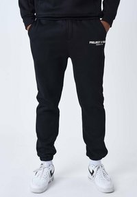 Pantalones deportivos negros de tejido suave, con cintura y puños elásticos, y con el logotipo blanco "PROJECT X PARIS" en la cadera izquierda.
