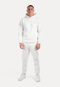 Felpa bianca con tasca a marsupio, abbinata a joggers bianchi e sneakers bianchi. Design minimalista, tessuto morbido, forma aderente.