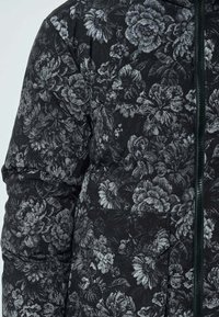 Veste rembourrée à motif floral en noir et gris, dotée d'une fermeture éclair, d'un tissu texturé et d'une poche sur le côté.
