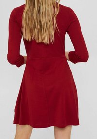 Czerwona sukienka z długim rękawem, dopasowaną górą i rozkloszowanym dołem, wykonana z miękkiego materiału jersey, charakteryzująca się gładką teksturą i prostym wzornictwem.