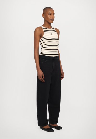 Top sin mangas a rayas en color crema con rayas negras, combinado con pantalones de mezclilla negros de talle alto. El modelo lleva zapatos planos negros.