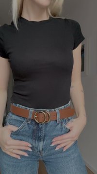 Brun läderbälte med rund guldfärgad spänne bärs över högmidjade ljusblå denimjeans. Svart åtsittande t-shirt täcker överkroppen.