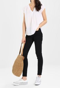 Vit kortärmad topp med V-ringning, svarta smala jeans, vita sneakers och en vävd beige handväska. Enkelt mönster och avslappnad passform.