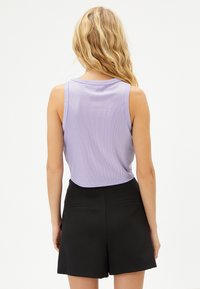 Lila ribbad ärmlös topp med en kortad design, tillsammans med höga svarta shorts med bakfickor.