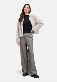 Lichtgrijze nepbontjas, zwart getailleerd shirt en wijdvallende grijs-geblokte broek met een trekkoord. Chunky zwarte schoenen maken de outfit compleet.