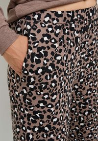 Jogging en imprimé léopard marron, avec des taches noires et blanches, en coton doux, et poches latérales. Taille élastique pour un confort optimal.