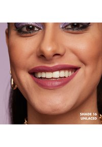 Läppstift i nyansen 16 "Unlaced", matt finish, djup mauve färg. Modellen visar ett närbildssmiles med tydligt definierade läppar och naturliga tänder.