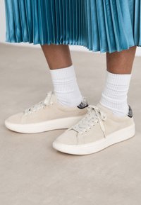 Person wearing white sneakers, white crew socks, and a pleated blue midi skirt standing on a light floor.