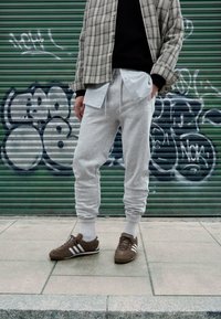 Szare spodnie dresowe z prążkowanymi ściągaczami i sznurkiem, nałożone na niebiesko-białą pasiastą koszulę, w połączeniu z brązowymi butami sportowymi z białymi akcentami.