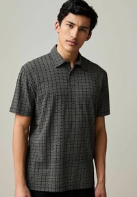 Camicia a maniche corte bianca e nera con un motivo geometrico a quadrati, design con colletto e una texture del tessuto morbida.