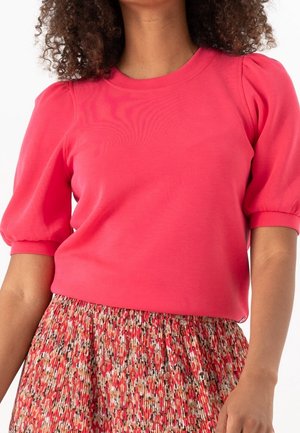 Top de manga abullonada rosa hecho de tela suave, combinado con una falda texturizada con estampado floral en tonos rojos, rosas y colores neutros.