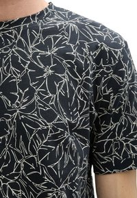 T-shirt noir avec un motif floral blanc, confectionné en tissu doux. Les manches courtes et le col rond complètent son design.