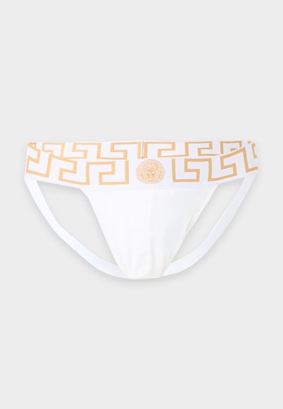 Slip bikini blanc pour homme avec un motif clé grec doré et un logo tête de Méduse sur la ceinture, sur un fond uni.