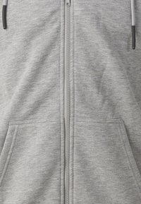 Grå zip-up hættetrøje lavet af blød, tekstureret stof. Har en frontlynlås og to sidelommer, med snøre detaljer ved hætten.