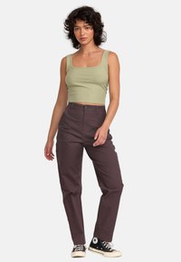 Olivovo zelený rebrovaný crop top spárovaný s nohavicami s vysokým pásom v tmavo fialovej farbe a čiernymi teniskami. Oblečenie má voľný strih a minimálne detaily.