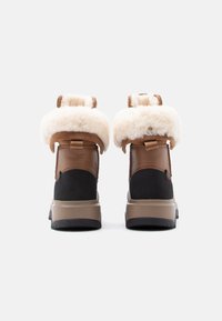 Waterdichte laarzen van bruin leer en zwart suède met weelderige witte bontboorden, stevige beige rubberen zolen en aantreklussen voor gemakkelijk aan- en uittrekken.