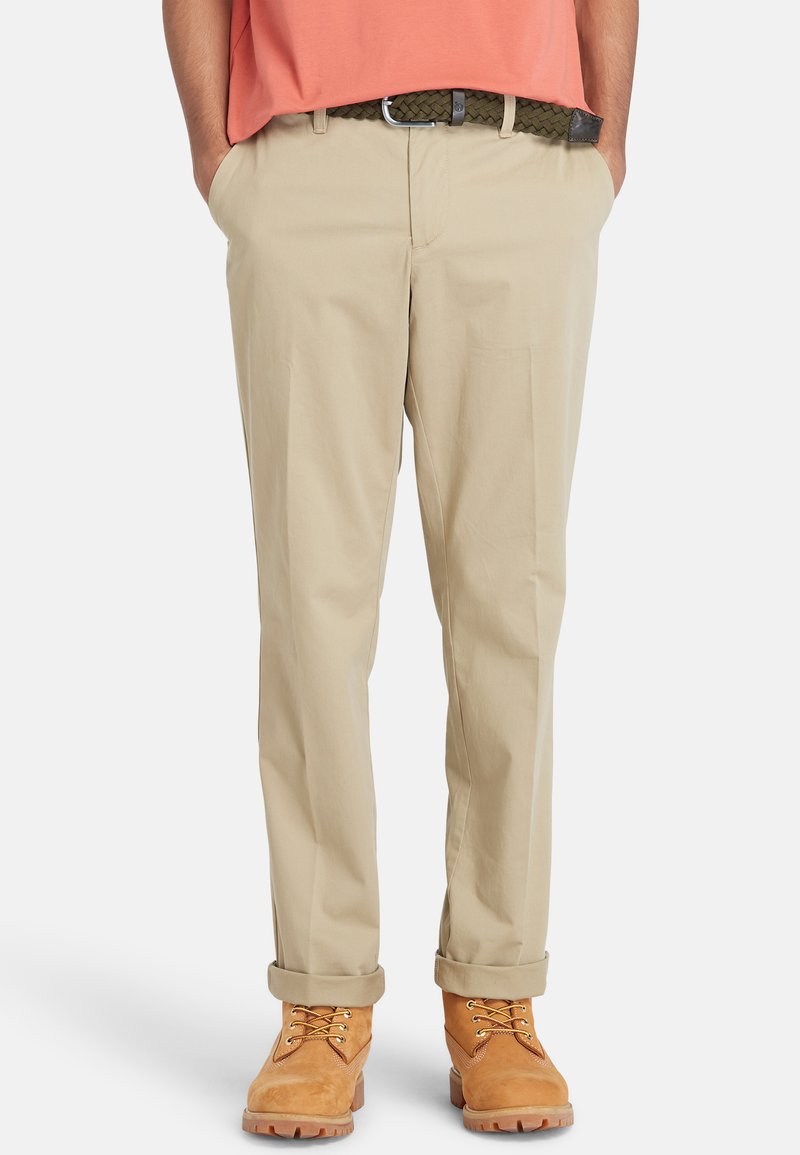 Chino in cotone beige, design a gamba dritta, orlo risvoltato, tasche frontali, indossati con una cintura intrecciata e stivali da lavoro beige.