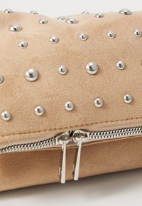 Bežna clutch torbica od lažne suede kože s ukrasnim srebrnim zakovicama i srebrnim zatvaračem. Tekstura površine sa okruglim metalnim akcentima i detaljima šivanja.