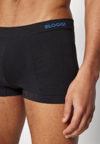Schwarze Boxershorts aus einem weichen Stoff, mit einem blauen "SLOGGI"-Logo am Bund und einer engen Passform mit geripptem Muster an den Seiten.