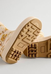 Bottes en caoutchouc à motif floral avec une base beige ; semelles texturées et flexibles présentant un profil zigzag et des accents circulaires pour une meilleure traction.