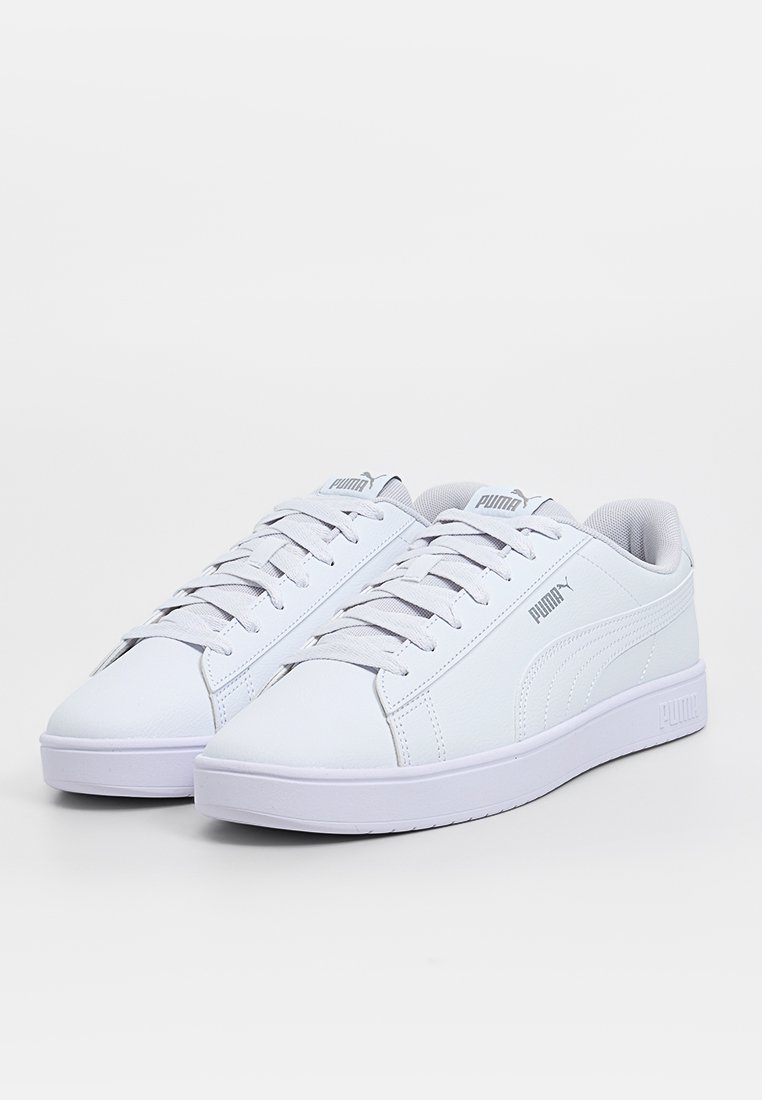 Zapatillas deportivas blancas de material sintético con diseño de bajo corte, que presentan una superficie texturizada, cierre con cordones y un detalle de logo.