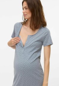 Gravid kvinna som bär en blå mönstrad ammningsnattklänning och knäpper upp bröstpartiet för att få tillgång till amning.