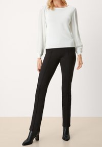 Pull gris clair avec manches ballon plissées, associé à un pantalon noir ajusté avec des coutures apparentes et des bottines noires.