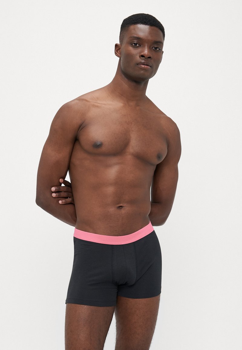 Boxeri negri din bumbac cu un brâu elastic roz, confecționați dintr-un material moale, care evidențiază o siluetă ajustată și o textură netedă.