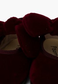 Bordeaux fluwelen schoenen met een ronde neus, voorzien van een opvallende strikaccent op elke schoen en een gestructureerde rand langs de zijkanten.