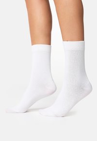 Hvide bomuldsokker med ribbede manchetter, der har en glat tekstur og en længde til midt på læggen. Sømfri design ved tåområdet for øget komfort.