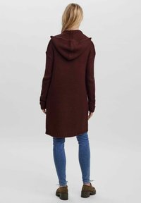 Burgundy knitted cardigan with a hood, long sleeves, ribbed cuffs and hem, paired with blue jeans and brown shoes, set against a plain background.
