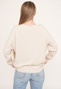 Beige übergroßer Pullover mit Rundhalsausschnitt und langen Ärmeln, aus weichem Stoff gefertigt. Die Rückseite hat ein einfaches Design mit geripptem Saum.