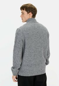 Grijze gebreide trui met een hoge kraag, textuurpatroon, ribbels aan de mouwen en zoom. Bevat kabels over de schouders, gemaakt van zachte stof.