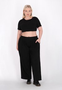 Sort cropped t-shirt med korte ærmer, der er parret med løse sorte bukser med elastisk talje og to sidelommer. Sorte støvler fuldender outfittet.