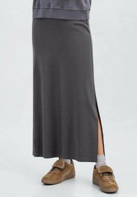 Siva duga suknja od mekanog materijala s bočnim prorezom, uparena s smeškastim tenisicama na čičak i belim čarapama do gležnja.