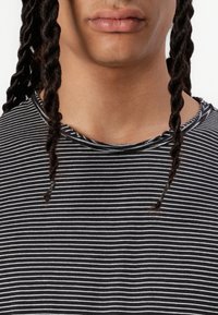 Black and white striped shirt with a rounded neckline and frayed collar. Visible braids frame the neck area. Soft cotton material.