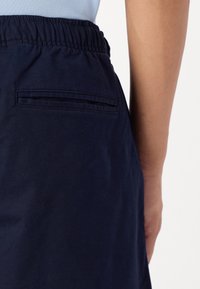 Shorts avec taille élastique bleu marine présentant une poche arrière. Le tissu semble lisse avec un léger éclat et des détails de couture durables.