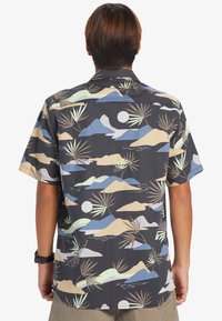 Koszula z krótkim rękawem z ciemnym tłem i wzorem gór oraz liści palmowych w delikatnych kolorach, wykonana z lekkiego materiału.