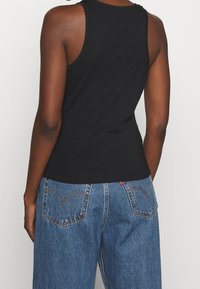 Svart ärmlös tanktop med rund halsringning. Kombinerat med ljusblå högmidjade jeans som visar detalj av sömnad på bakfickan.