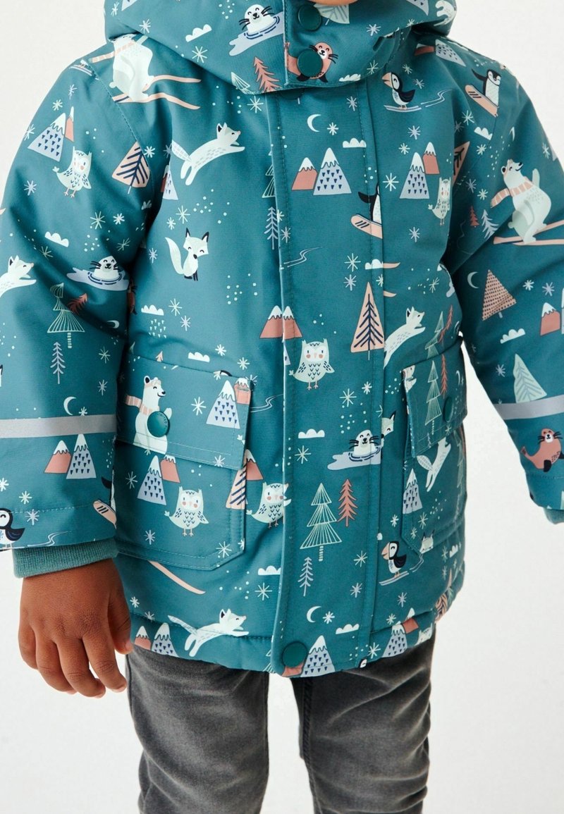 Enfant portant une veste d'hiver bleu sarcelle avec des motifs d'animaux de la forêt et de la montagne, incluant des renards, des hiboux, des ours polaires et des phoques.