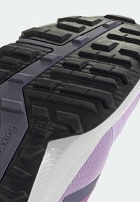 Podešev boty s černou gumovou plochou se silnými výstupky pro lepší trakci, texturovanou fialovou střední částí podrážky a akcenty v kontrastních barvách.
