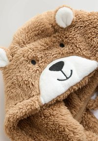 Braunplüsch-Bärenkapuze mit gestickten schwarzen Augen, einer Nase und einem lächelnden Mund auf einer weichen weißen Schnauze, Teil eines flauschigen Gewandes oder einer Decke.