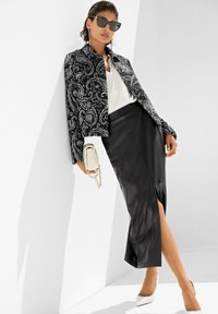 Schwarz-weiße, paisley-musterte, kurze Jacke, elegante schwarze Lederrock mit einem Schlitz vorne, weißes Oberteil und weiße spitze Heels.