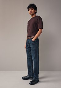 Ciemnobrązowy t-shirt z krótkim rękawem w połączeniu z niebieskimi jeansami. Czarne obuwie na masywnej podeszwie dopełnia strój. Prosty i casualowy design.